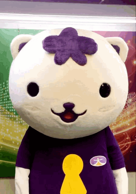 a stuffed animal with a purple flower on its head is wearing a purple shirt
