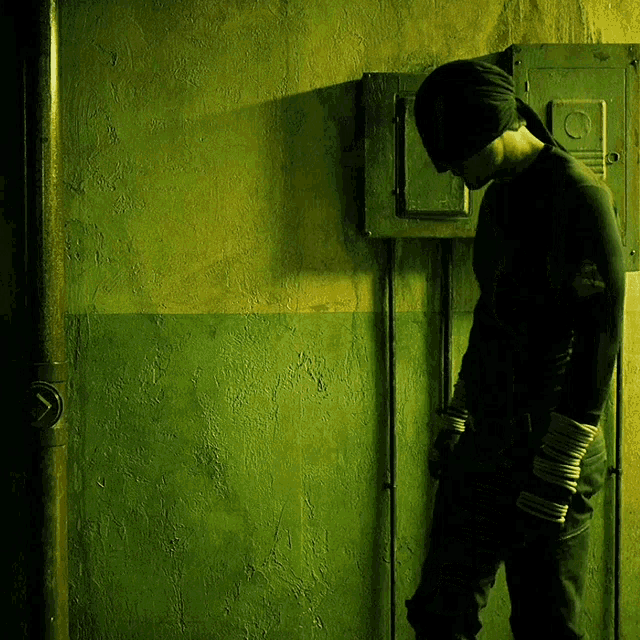 a man in a mask stands in front of a green wall with the letter c on it