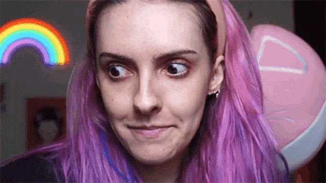 a woman with purple hair is making a funny face in front of a pink cat pillow .