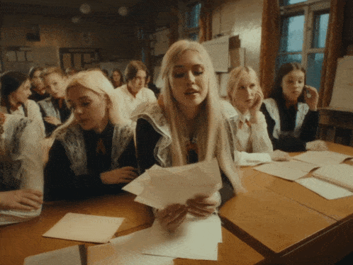 a group of girls are sitting at desks in a classroom looking at papers
