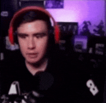 a man wearing headphones is sitting in front of a microphone and looking at the camera .