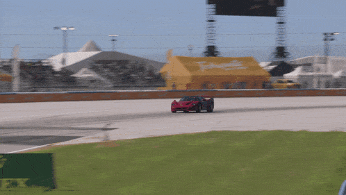 a red car is driving down a race track with a rolex sign in the grass