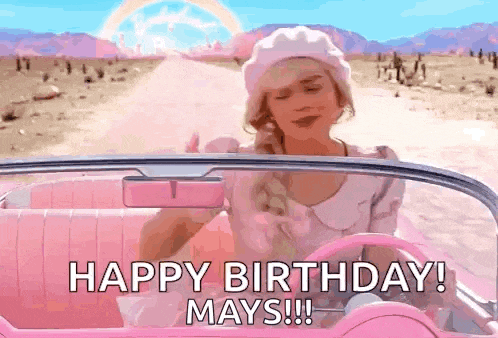 a woman is driving a pink car on a desert road and says `` happy birthday mays '' .