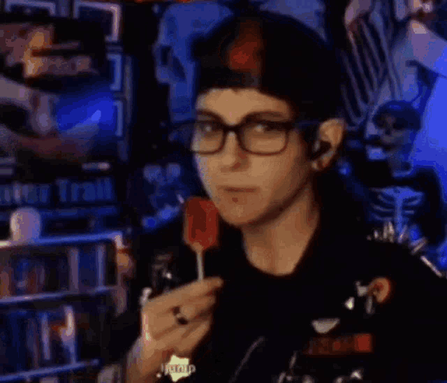 a woman wearing glasses and a hat is eating a lollipop in a dark room .