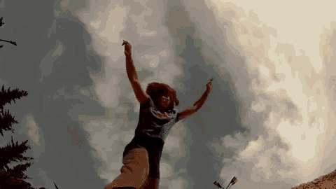 a person is jumping in the air with their arms outstretched in front of a cloudy sky .