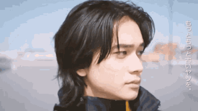 a young man with long black hair is wearing a black jacket and looking to the side .