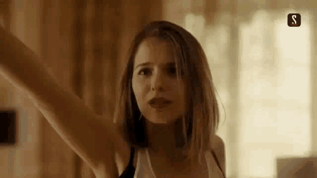 a woman in a white tank top is standing with her arms outstretched in a room .