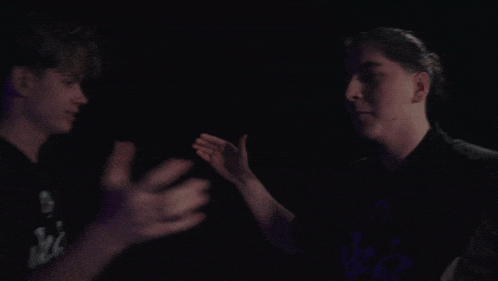 two men are fighting in a dark room with purple lights behind them .