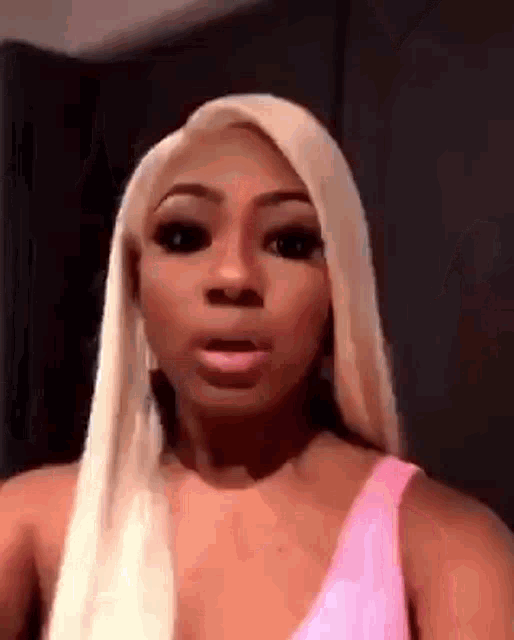 a woman with long blonde hair is wearing a pink tank top .