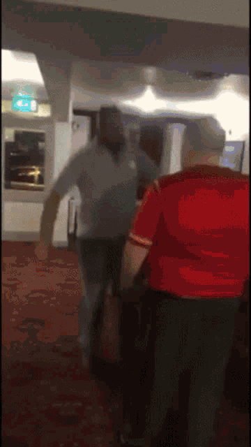 a man in a red shirt is standing next to another man on a red carpeted floor