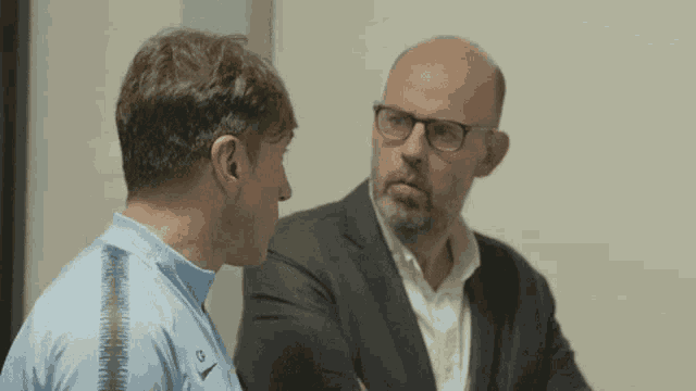 a man wearing a nike shirt talks to another man