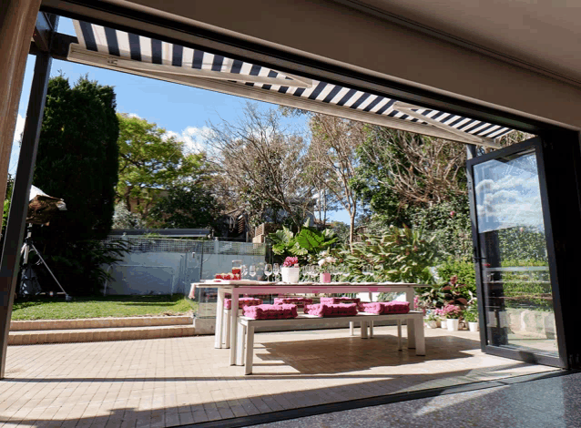 a patio with a table and benches and striped awning