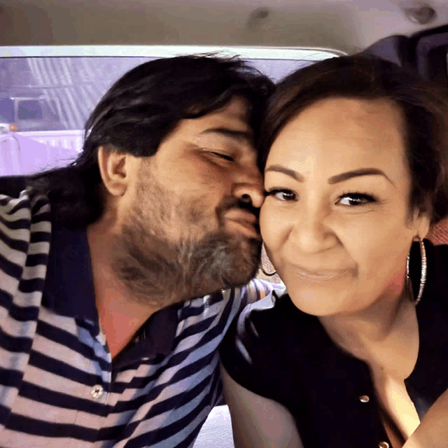 a man kisses a woman on the cheek in a striped shirt