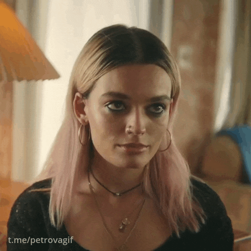 a woman with pink hair and hoop earrings looks at the camera