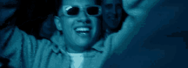 a man wearing glasses is covering his eyes with his hands in the dark .