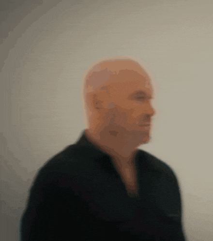 a bald man in a black shirt is standing in front of a wall