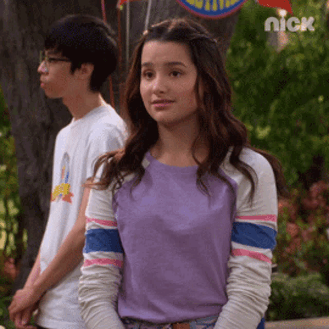 a girl in a purple shirt is standing next to a boy in a white shirt with nick on the bottom