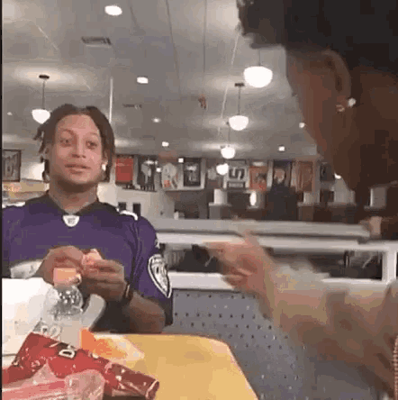 a man in a purple jersey is sitting at a table talking to a woman .