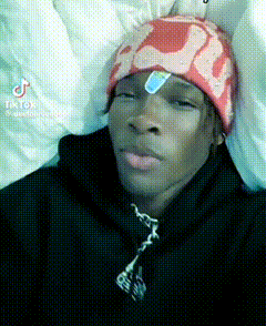 a young man wearing a red beanie and a black jacket is laying in bed with a bandage on his forehead .
