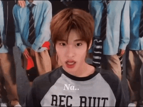a young man wearing a shirt that says rec butt is standing in front of a group of men in school uniforms .