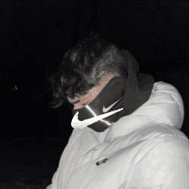a man wearing a white jacket and a black nike mask around his neck .