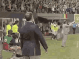 a man in a suit is standing on a soccer field with a crowd watching .