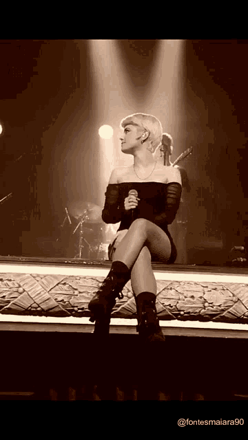 a woman is sitting on a stage holding a microphone with the words @ fontesmaiara90 below her
