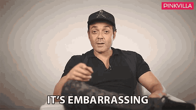 a man wearing a hat says it 's embarrassing while sitting in a chair