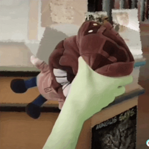 a green hand is holding a stuffed animal in front of a sign that says " auncle says "