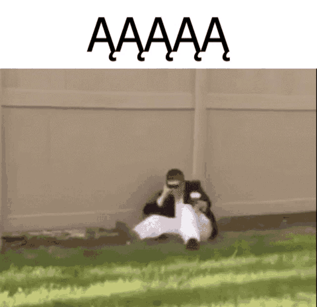 a man is sitting on the ground in front of a fence with the words aaaa written above him .