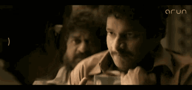 a man with a mustache is looking at another man in a dark room .