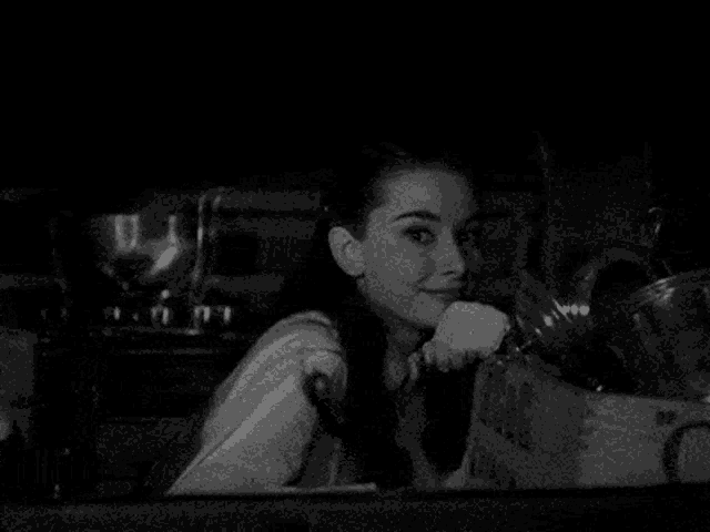 a woman is smiling in a black and white photo while looking out of a window in a kitchen .