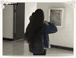 a woman with long black hair is standing in a hallway next to a fire extinguisher .