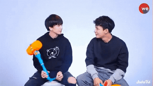 two young men are sitting next to each other holding balloons and talking to each other .