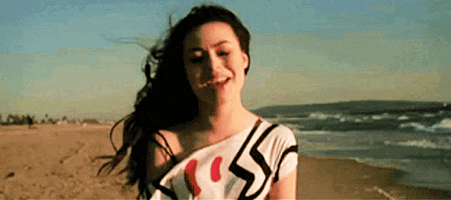 a woman is standing on a beach with her hair blowing in the wind and smiling .