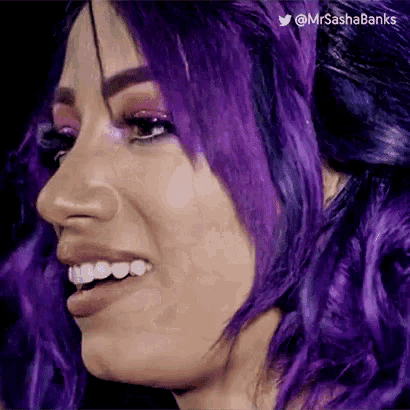 a woman with purple hair is smiling and looking at the camera .