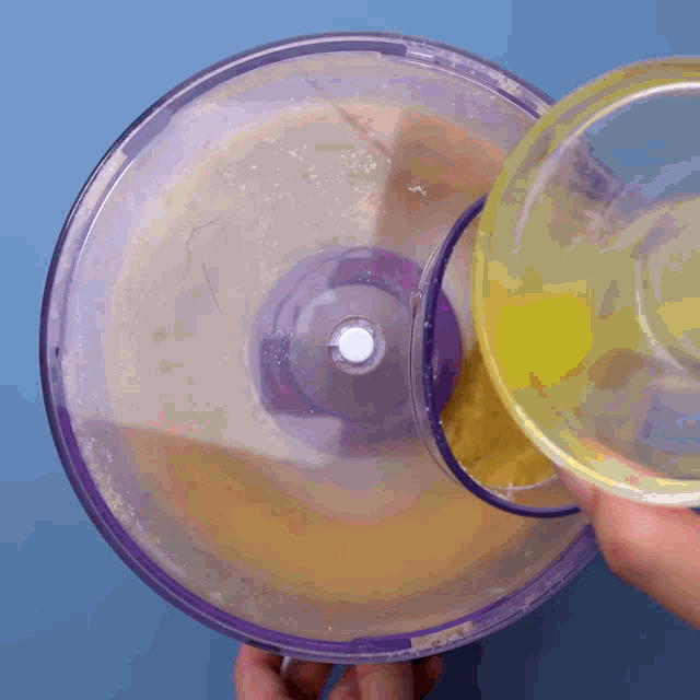 a person pouring liquid into a food processor with a blue background