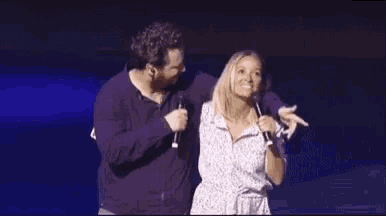 a man and a woman are standing next to each other on a stage . the woman is holding a microphone .