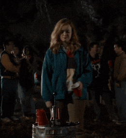 a woman in a blue jacket is standing next to a keg with a red cup in her hand