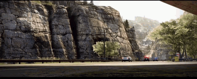 a few cars are driving down a road near a mountain