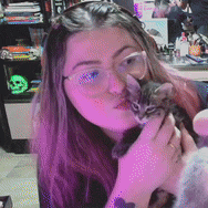 a woman wearing glasses is holding a kitten in her hands