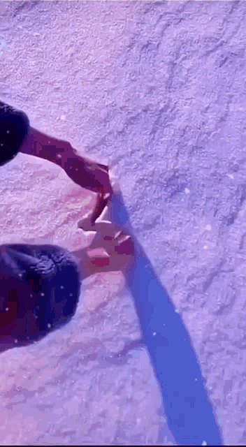 a person is holding another person 's hand in the snow and their shadow is visible .