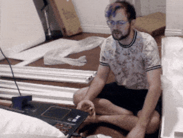 a man in a floral shirt sits on the floor with a laptop and a box that says ' ikea ' on it