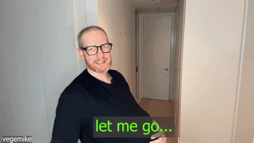 a man with glasses is standing in a hallway and says " let me go "
