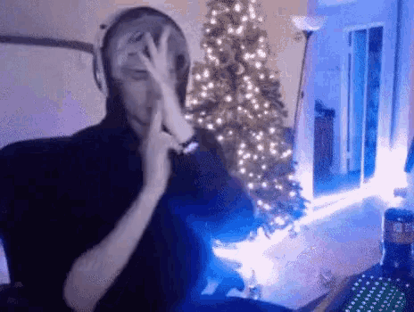 a man is sitting at a desk in front of a christmas tree and making a peace sign .