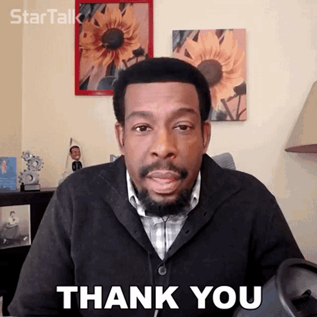 a man with a beard says thank you in front of a picture of sunflowers