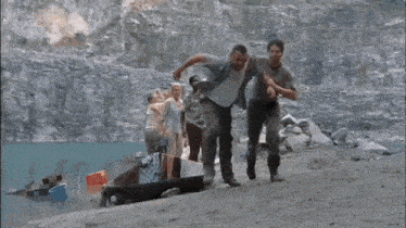 a man is laying on his back in the sand while a group of people are standing around him .