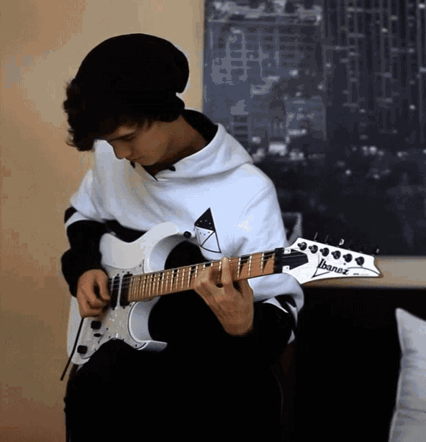 a young man is playing a white ibanez electric guitar