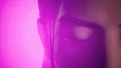 a close up of a woman 's face with purple lighting behind her .