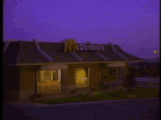 a mcdonald 's restaurant at night with a purple sky in the background